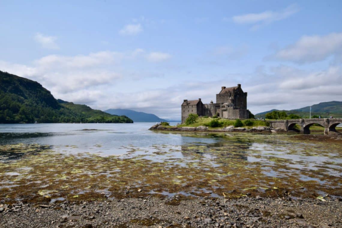 a rocky shore next to a body of water with a castle in the background